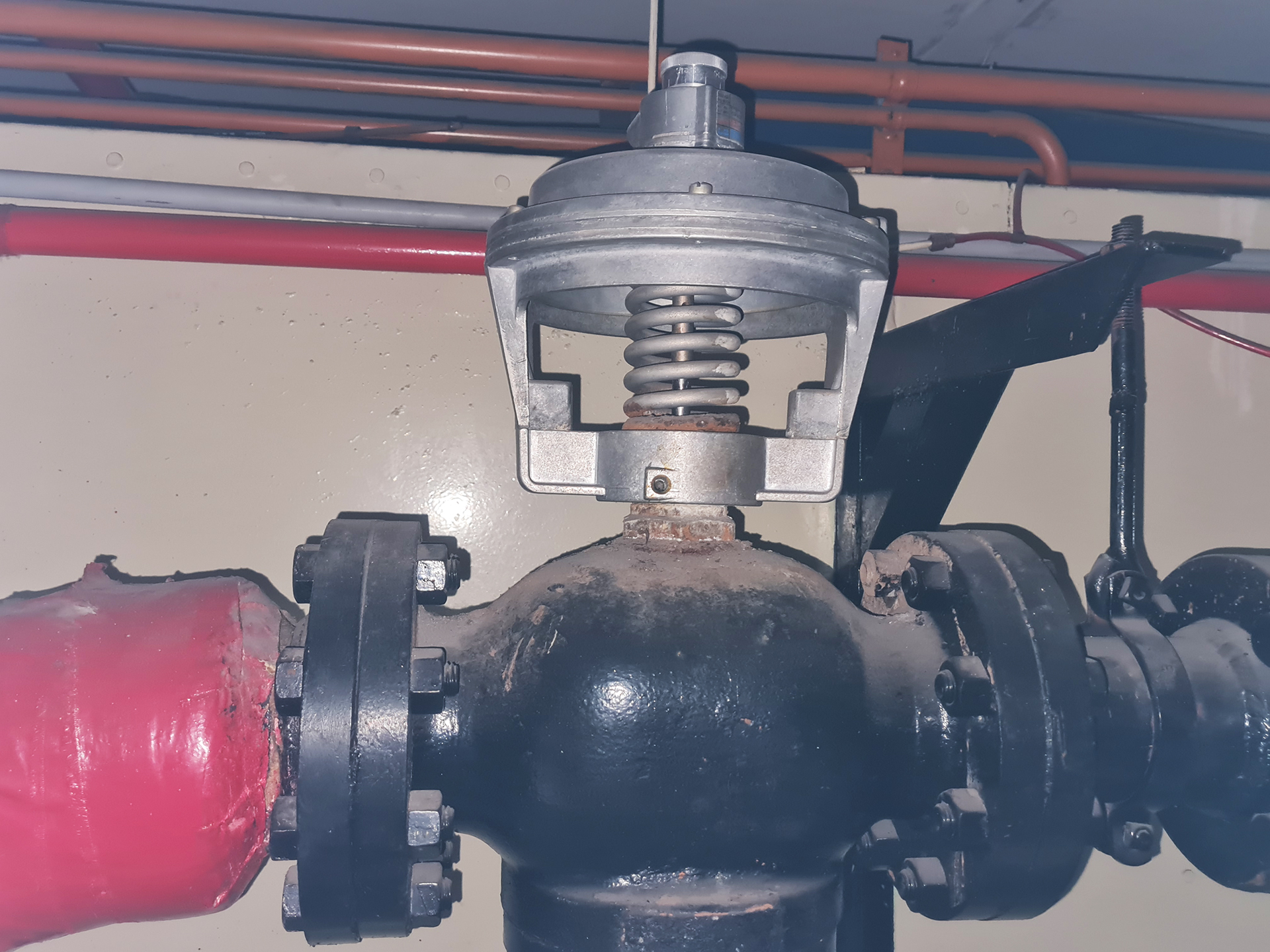 Two-Way Pneumatic Control Valve – Heating Hot Water System Two-way pneumatic control valve serving the Heating Hot Water system at a commercial property on Little Collins Street, Melbourne, Victoria. The valve is fitted with a spring-return pneumatic actuator and pressure gauge, allowing the control system to modulate heating hot water flow in response to building demand. In older commercial buildings, these pneumatic valve assemblies are often still operational but should be inspected for air leaks, actuator response, valve stroke, failed diaphragms, sticking stems, and correct control pressure. This type of legacy pneumatic HVAC equipment is common in Melbourne CBD buildings and can often be retained, repaired, calibrated, or progressively upgraded as part of a broader BMS or mechanical controls strategy.