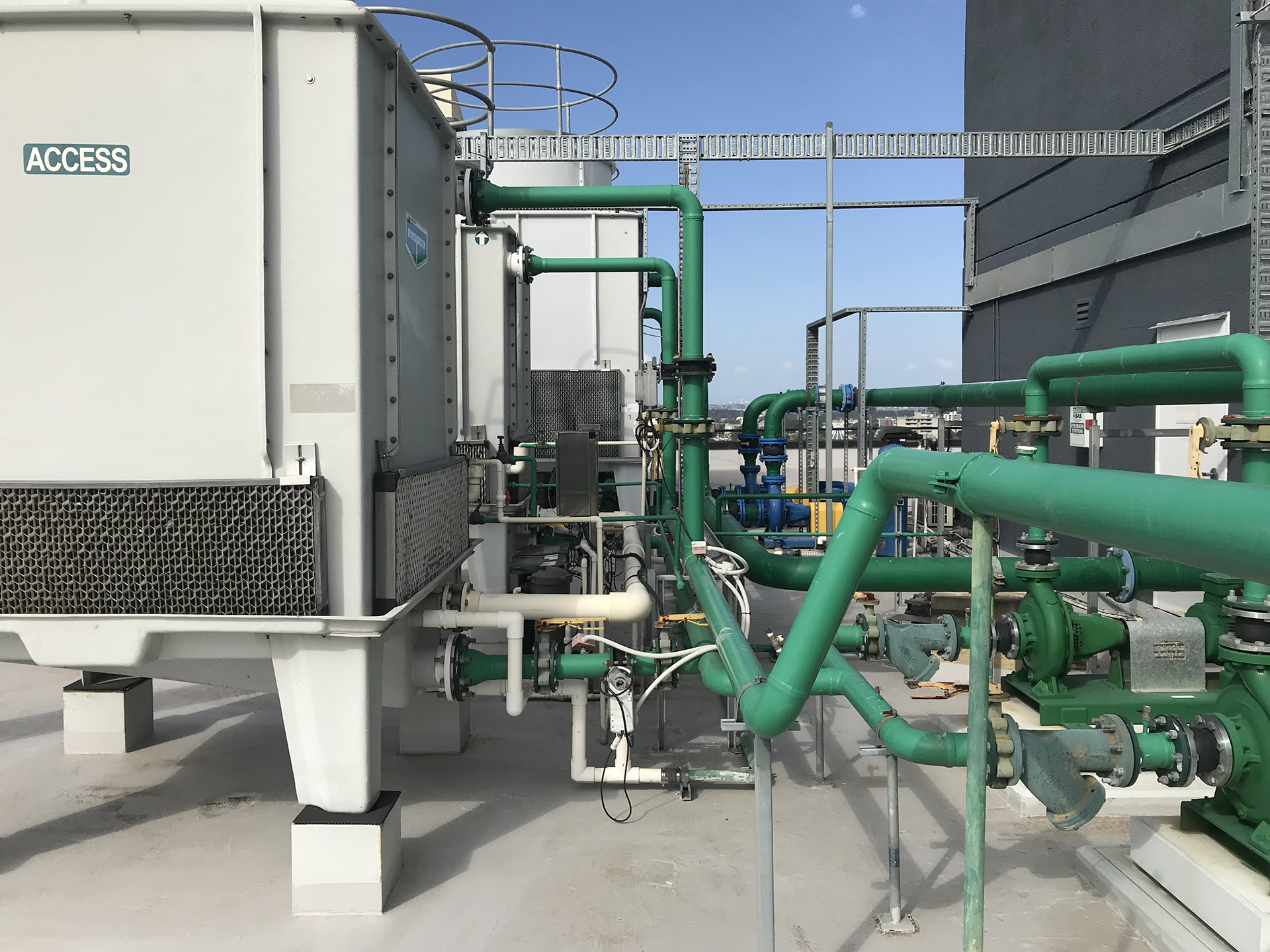 Large commercial HVAC condenser water infrastructure installed on a Sydney rooftop mechanical plant area, featuring cooling towers, condenser water pumps, extensive pipework, valves, and associated mechanical services equipment supporting central chilled water systems. The image demonstrates the complexity of HVAC power infrastructure and mechanical plant integration required within modern commercial buildings, including electrical motor control, Building Management Systems (BMS), Variable Speed Drives (VSDs), energy optimisation, and automated plant sequencing. WR8TECH specialises in integrated HVAC electrical infrastructure, plant automation, and smart building control systems across Sydney, Melbourne, and Canberra.