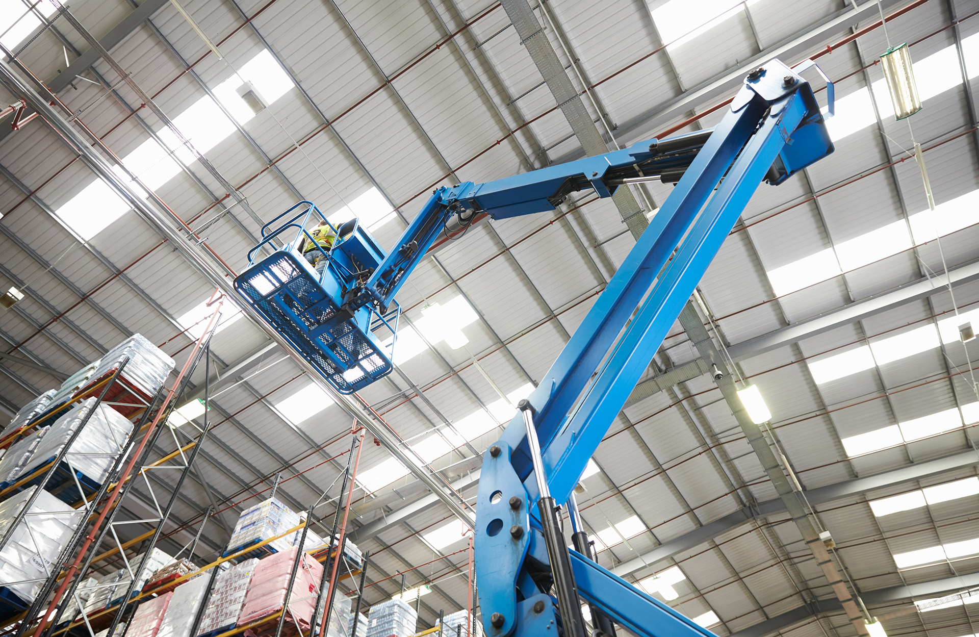 WR8Tech technician maintaining high-bay LED lighting in a commercial warehouse with translucent roof panels supporting daylight harvesting and energy-efficient lighting control.