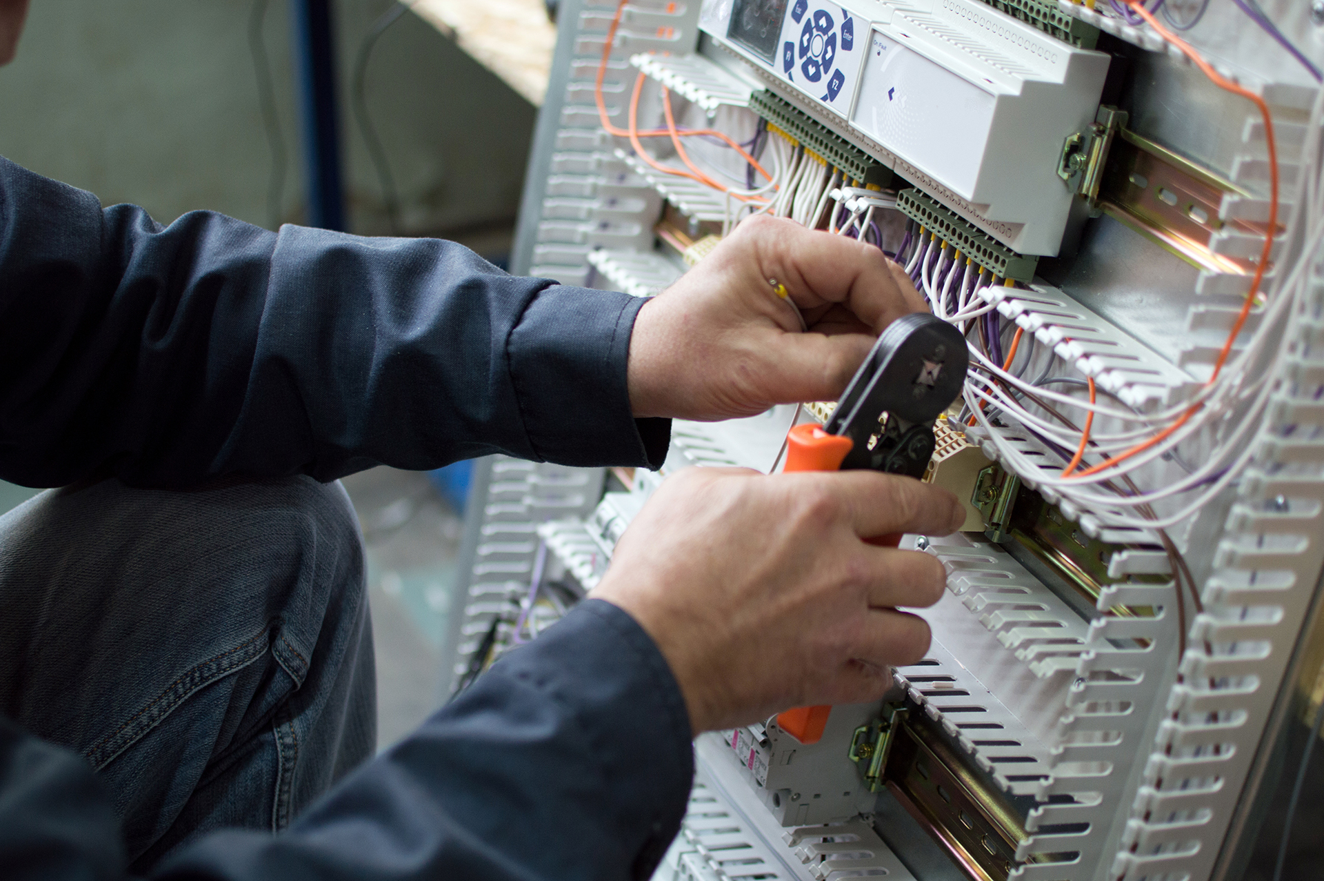 Technician wiring a Building Management System control panel while commissioning field devices and verifying the BMS Points List for commercial HVAC controls.