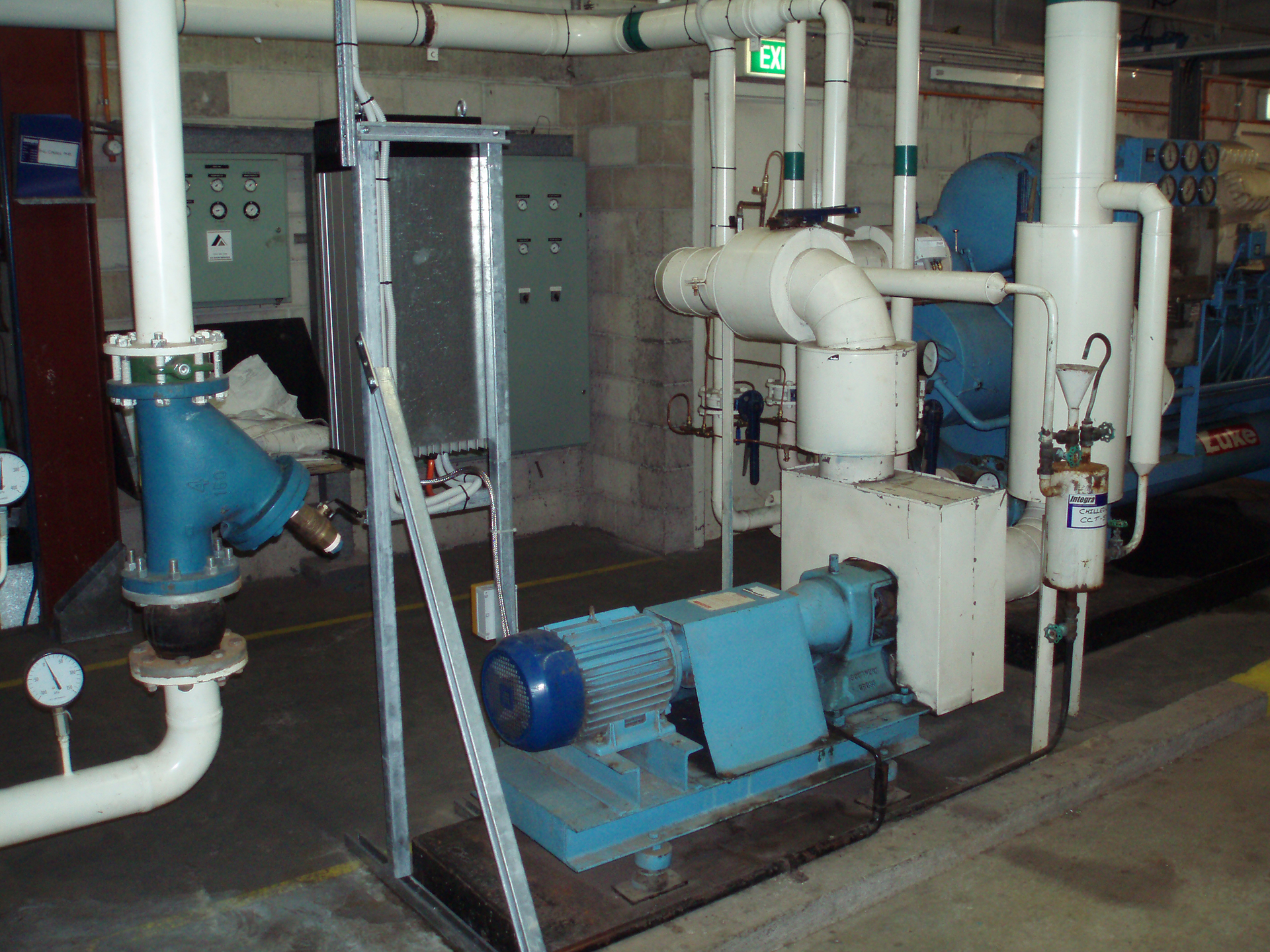 Commercial condenser water pump and pipework showing signs of deferred maintenance including deteriorated insulation, corrosion, worn paint and poor plant room condition.