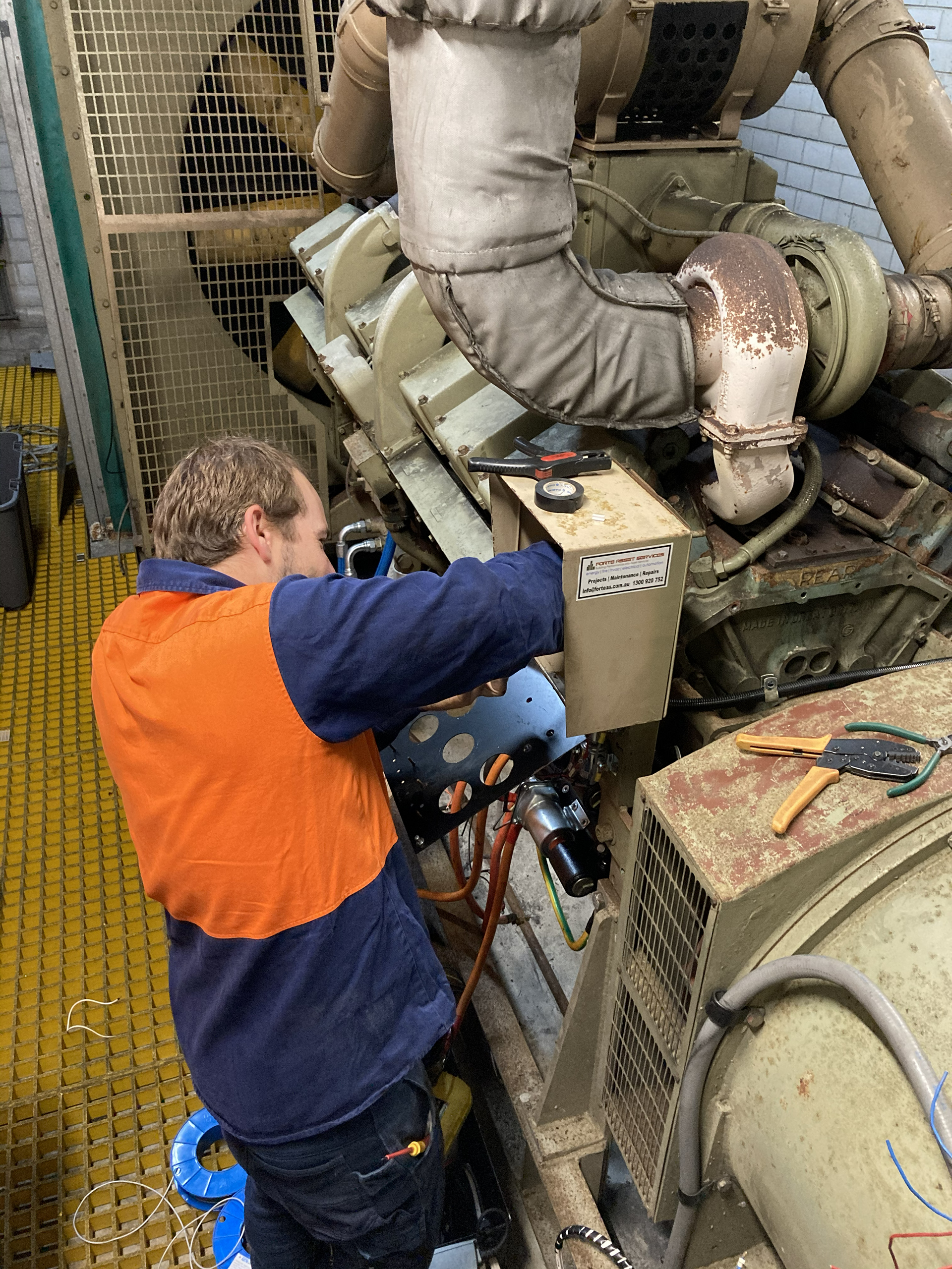 Technician servicing a diesel generator control panel on an essential services standby generator within a commercial building plant room in Sydney.