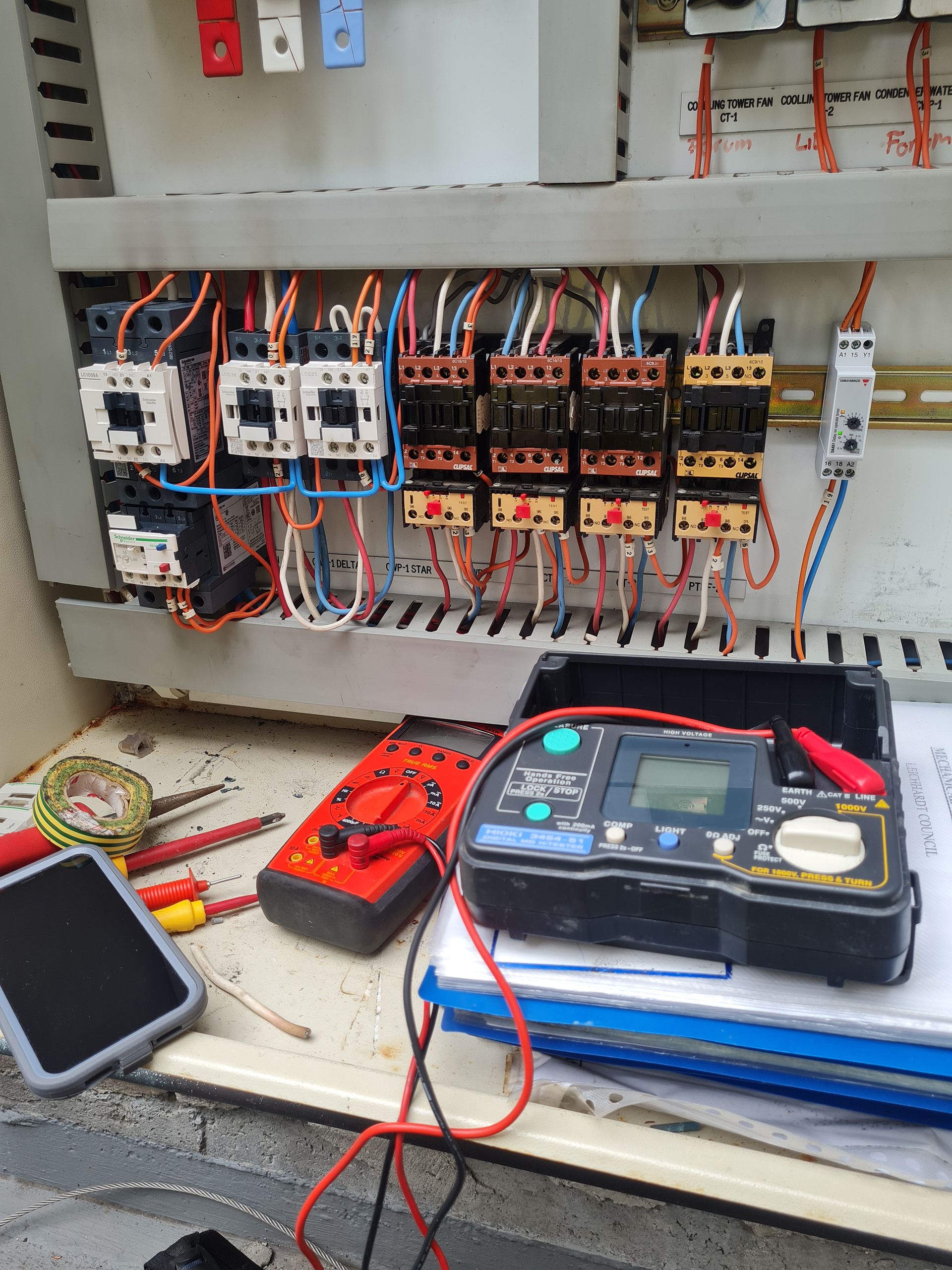 Engineer carrying out fault-finding and electrical testing inside a Mechanical Services Switchboard controlling cooling tower fans and condenser water pumps in a commercial building.