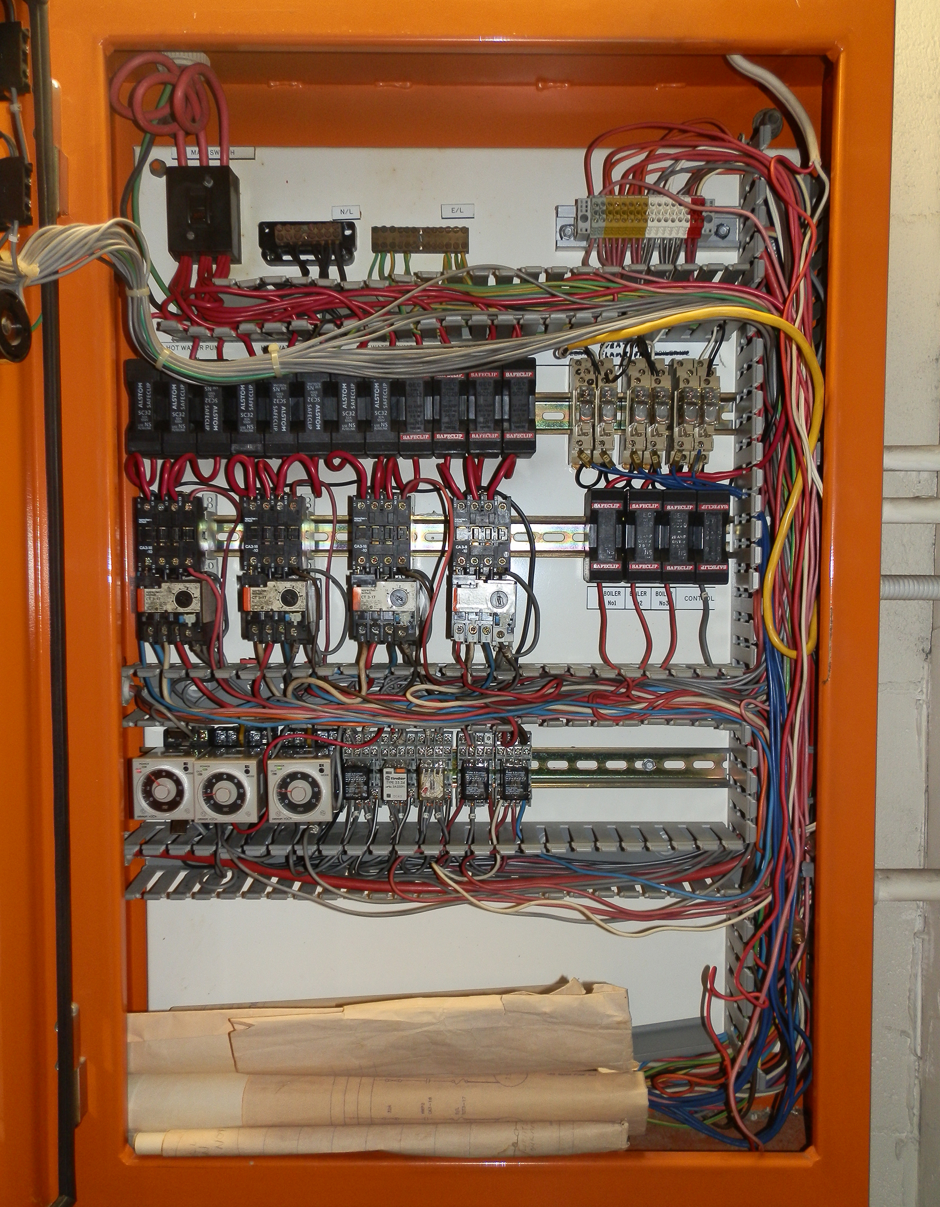 Older mechanical services control panel with ageing timers, HRC fuse holders, aged main switch, messy wiring and yellowed schematics.