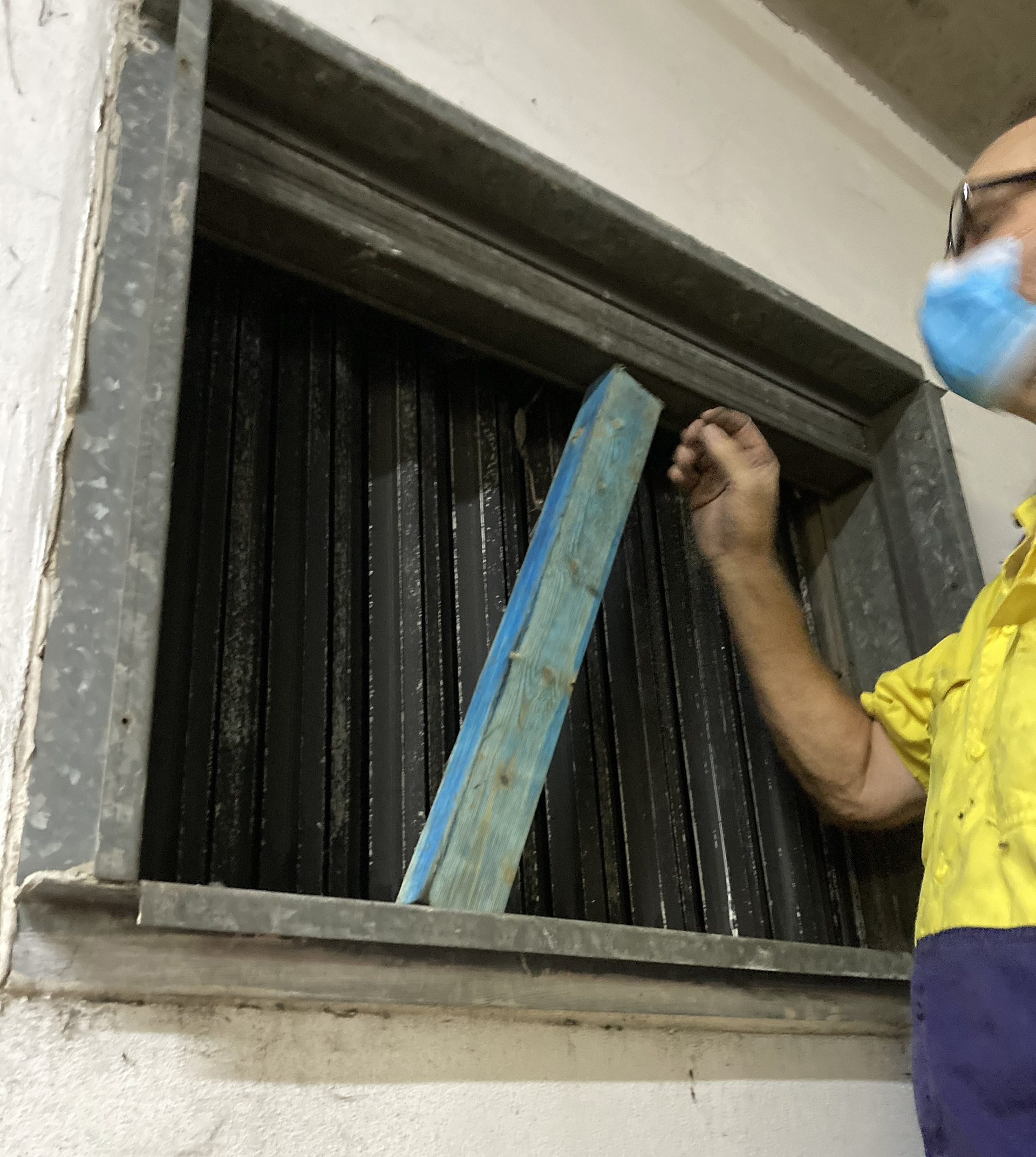 Technician inspecting a fire damper found improperly held open with a piece of timber during an HVAC audit.