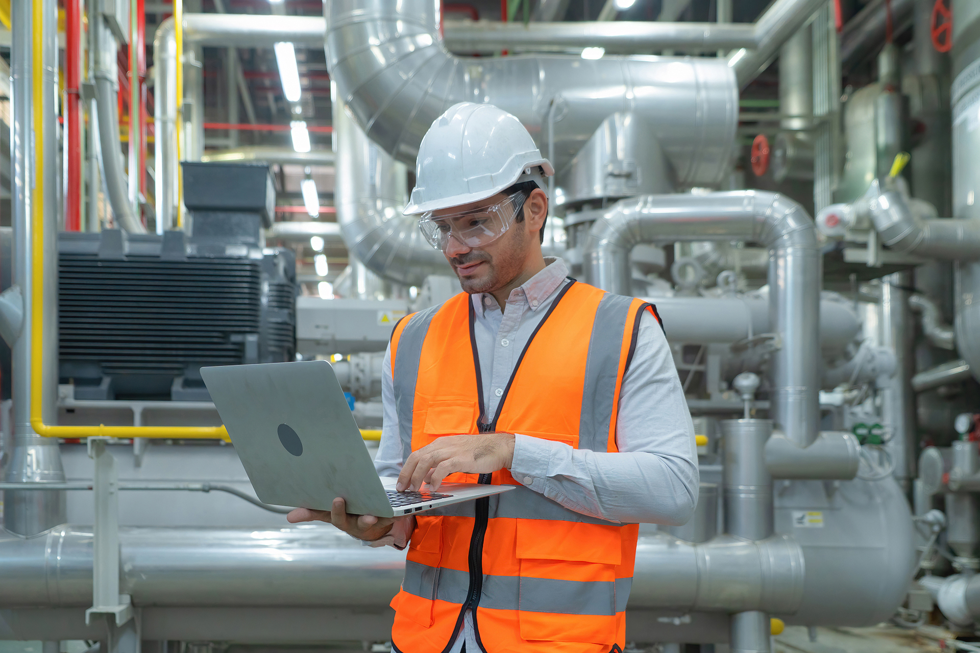Technical specialist inspecting commercial HVAC mechanical plant and recording audit findings on a laptop.